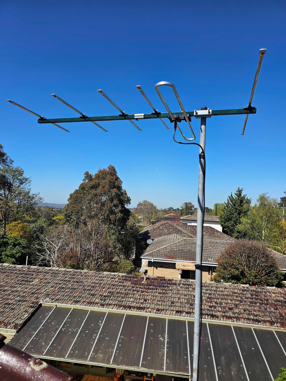 New Australian-made digital antenna installed on a galvanised mast above a tiled roof in Brunswick East under a clear blue sky