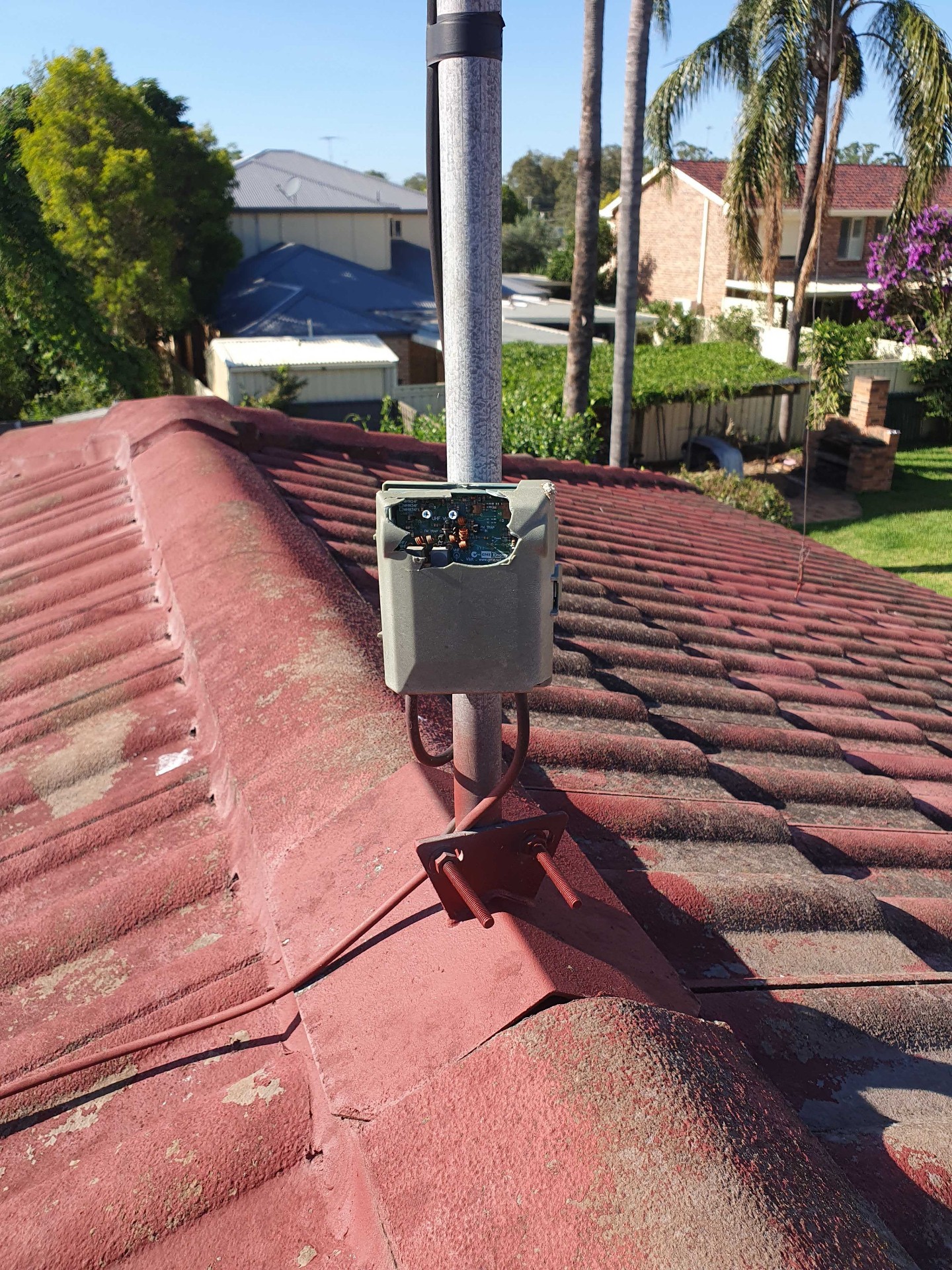 Damaged 25-year-old antenna amplifier with broken housing from bird and storm damage on a tiled roof in Emu Heights