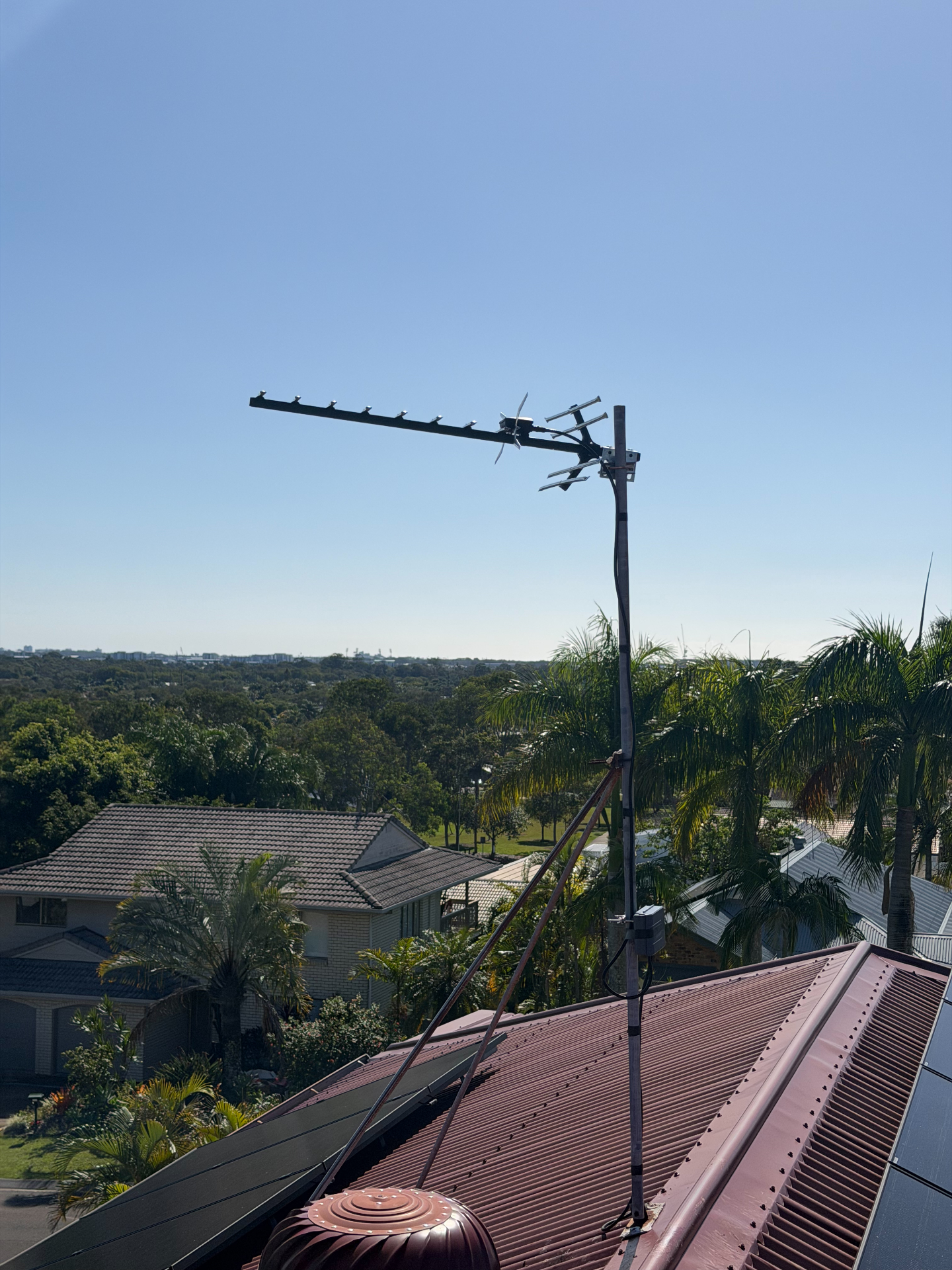 New Australian-made digital antenna installed on a rooftop mast in Murrumba Downs with clear blue sky and surrounding suburbs in the background